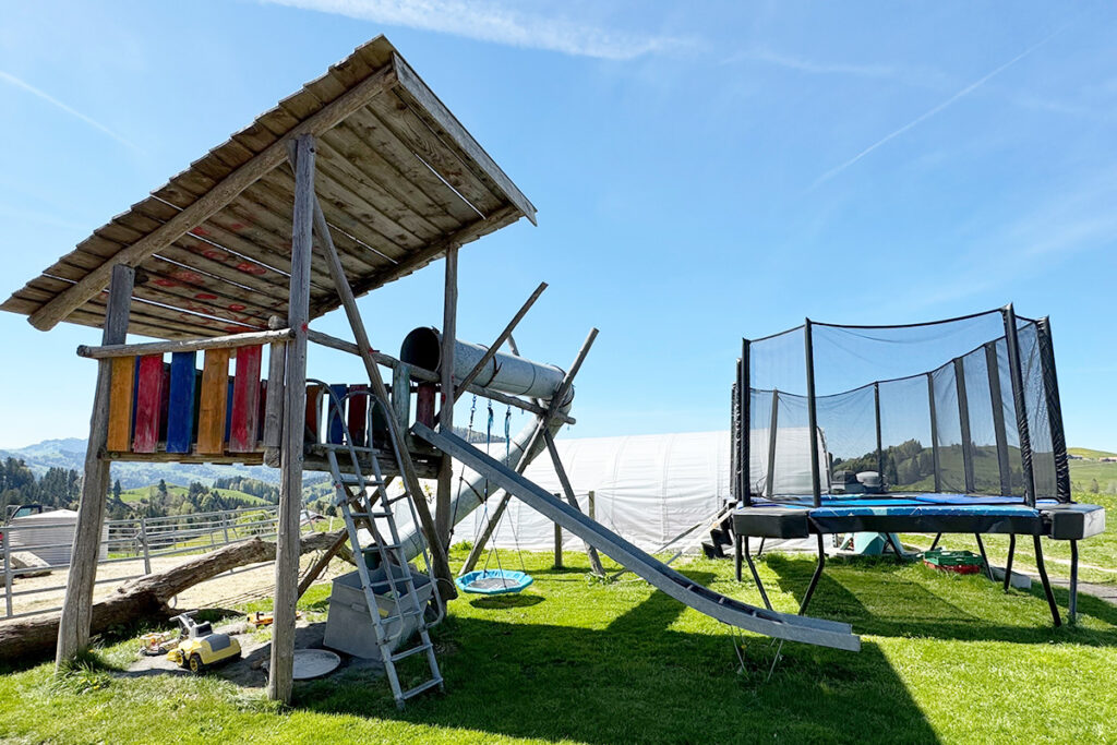 Spielplatz auf dem Alpakahof mit XXL Trampolin, Spielturm, Rutsche, Schaukel und Sandkasten für Kinder auf dem Bauernhof in der Schweiz
