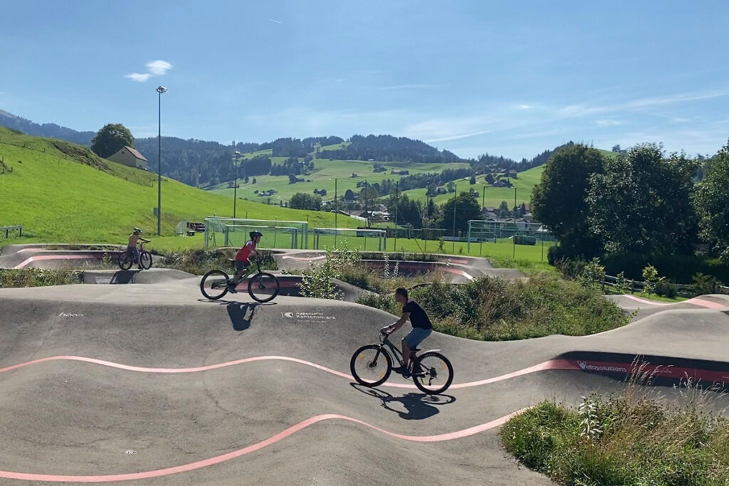 Pumptrack Urnäsch mit Familie beim Velofahren vor der Hügellandschaft des Appenzellerlands
