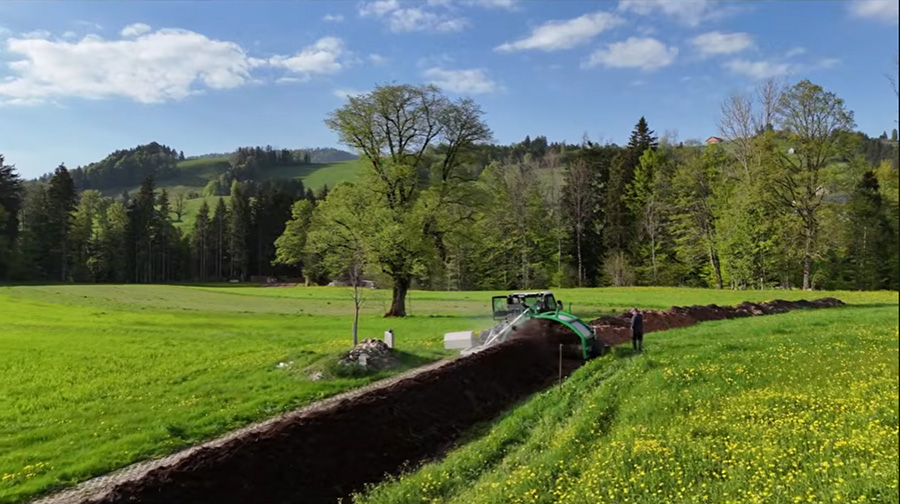 Drohnenaufnahme der Mistaufbereitung mit Aebi Transporter und Gujer Kompostwender bei Christian Müller in Bächli-Hemberg, umgeben von grünen Frühlingswiesen und Hügeln.