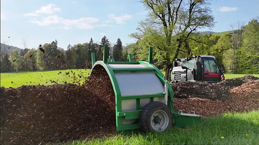 Seitenansicht der Mistaufbereitung mit Gujer Kompostwender und Aebi Vario VT 450, während Hackschnitzel und Mist homogen vermischt und hinter der Maschine ausgeworfen werden.